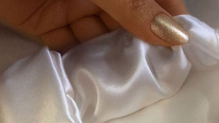 Close-up of hand touching smooth white mulberry silk fabric highlighting soft luxurious texture