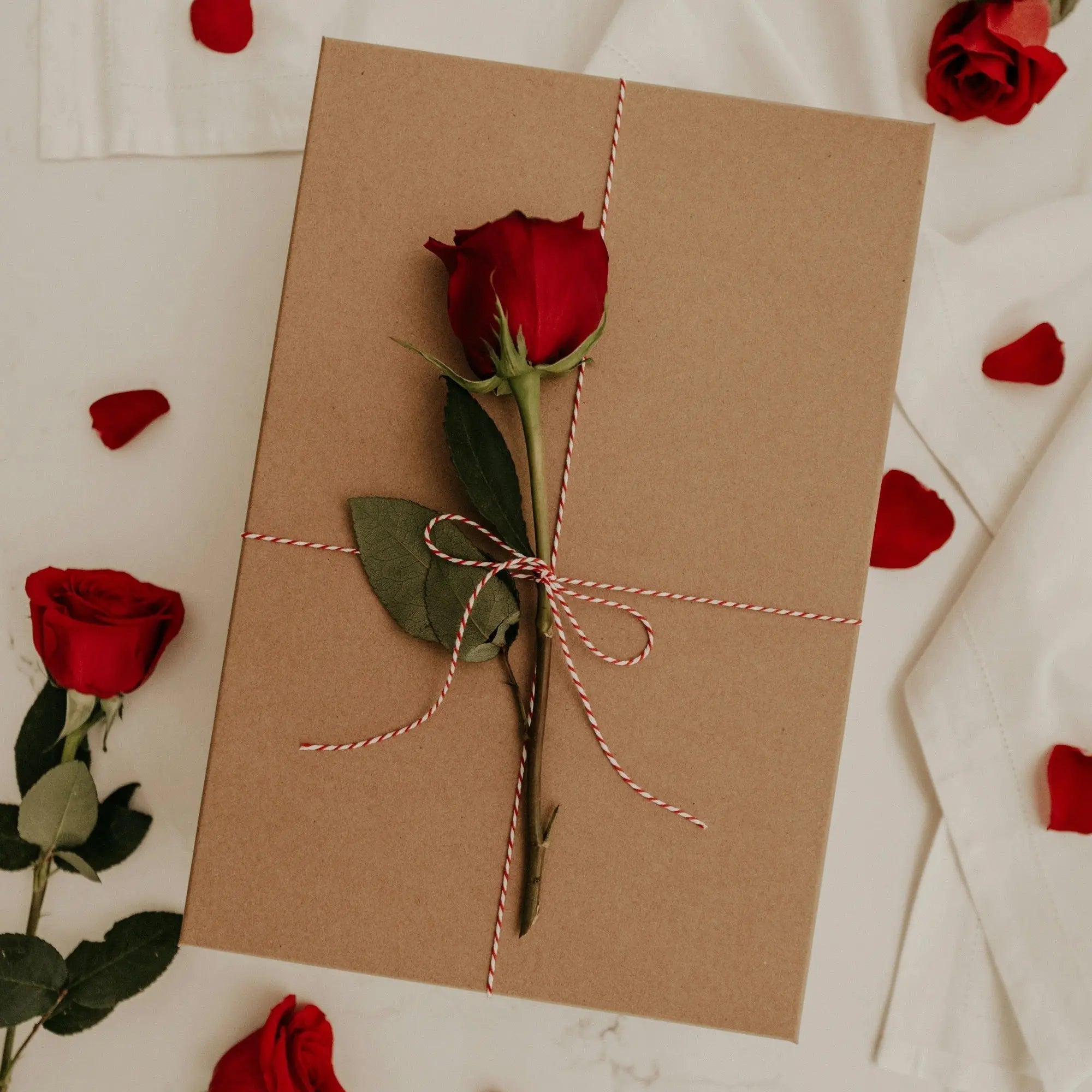 Minimalist Valentine's Day gift box in sustainable kraft paper tied with baker's twine and a fresh red rose for thoughtful gifting inspiration.