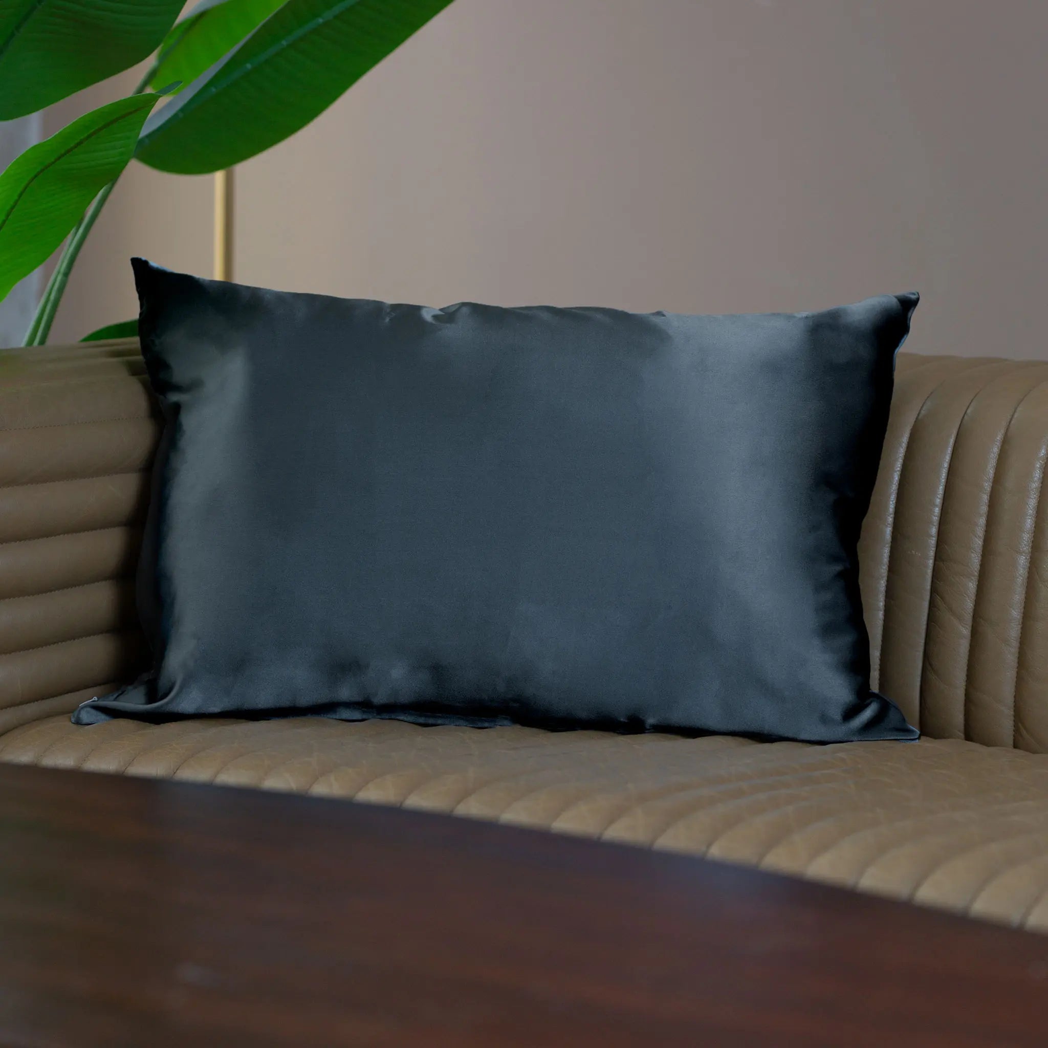 Pillow with Black Beauty silk pillowcase on a beige leather sofa couch with a plant in the background styled in modern contemporary setting— Silk Souq pure mulberry silk home decor.