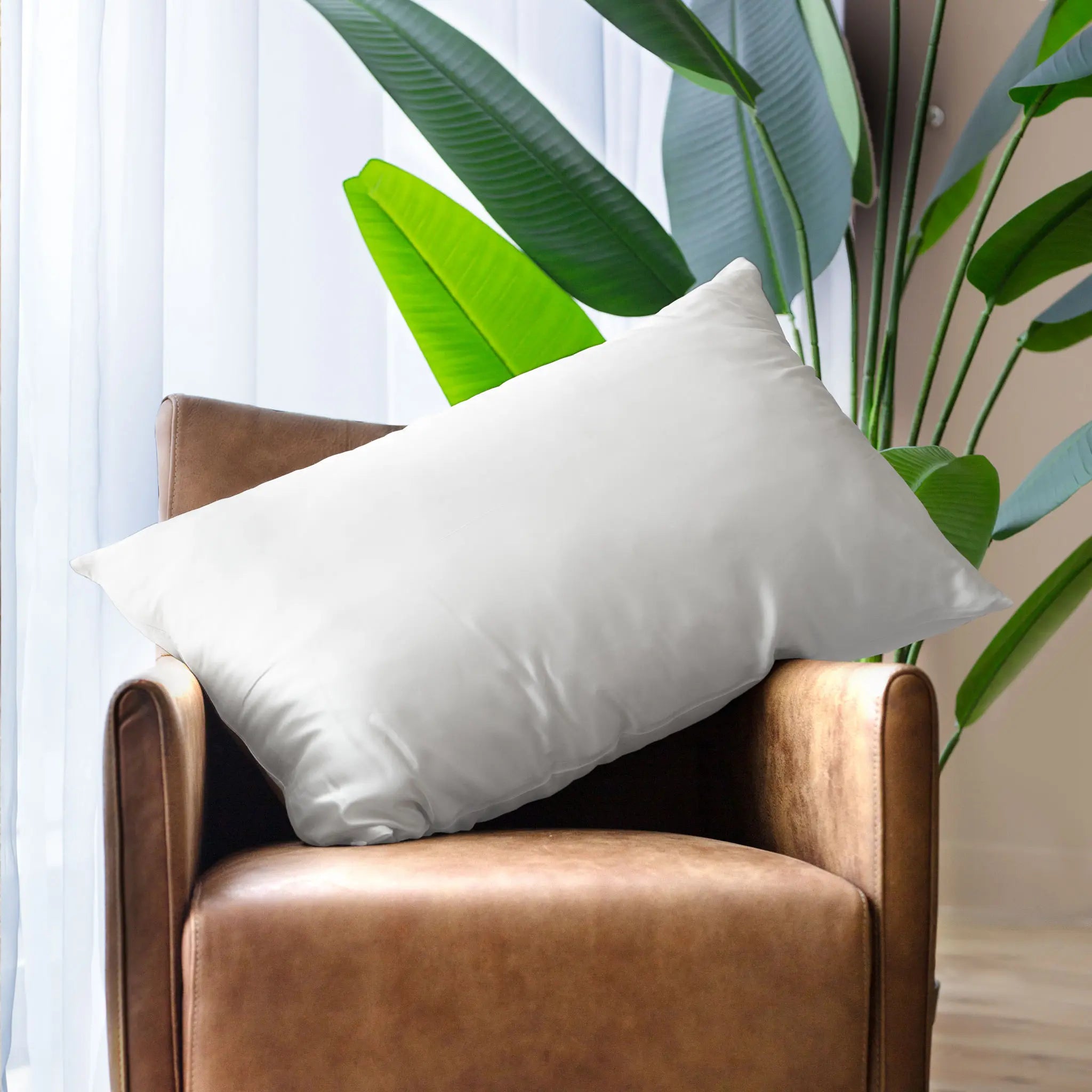 Pillow with Ivory White silk pillowcase styled on a brown leather arm chair with a plant in the background — Silk Souq pure mulberry silk home decor.