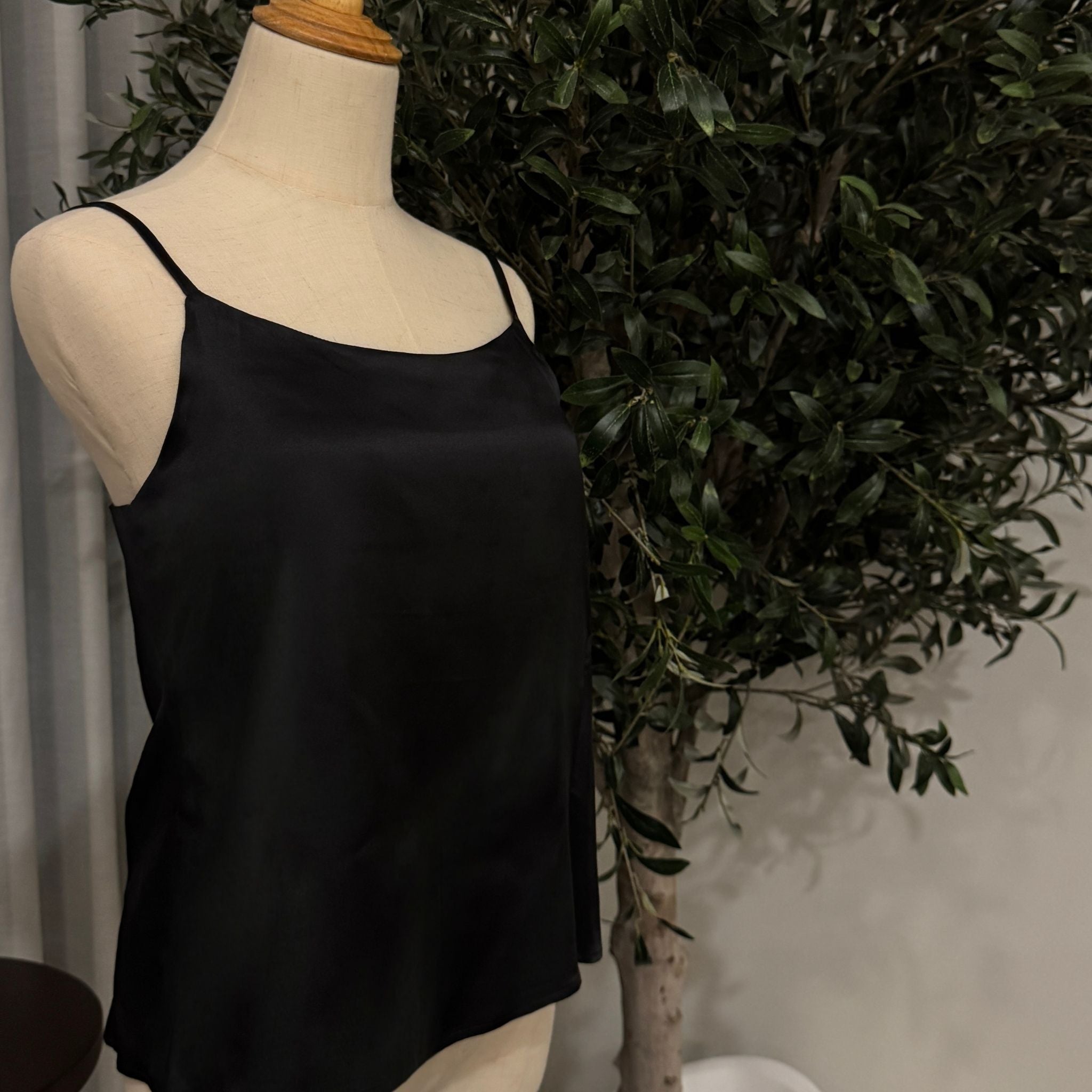 Black spaghetti strap top on a mannequin against a green plant background