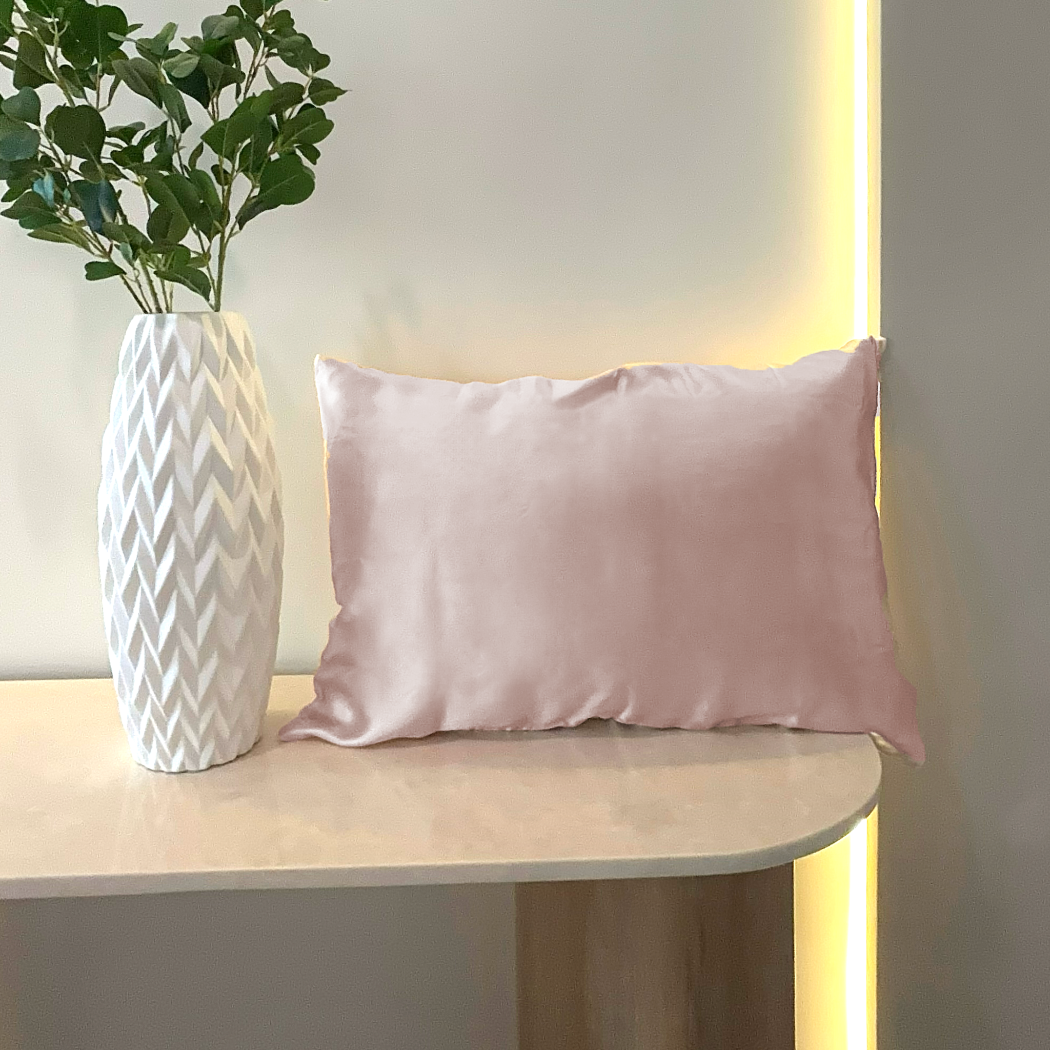 Pillow with Soft Blush silk pillowcase  on a marble surface with a white vase containing greenery against a neutral wall.  — Silk Souq pure mulberry silk home decor.