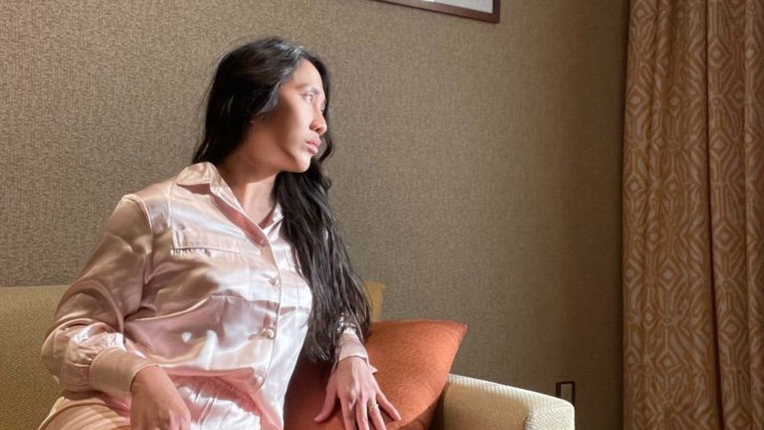 Founder Aizza wearing silk pajamas on a well-lit couch