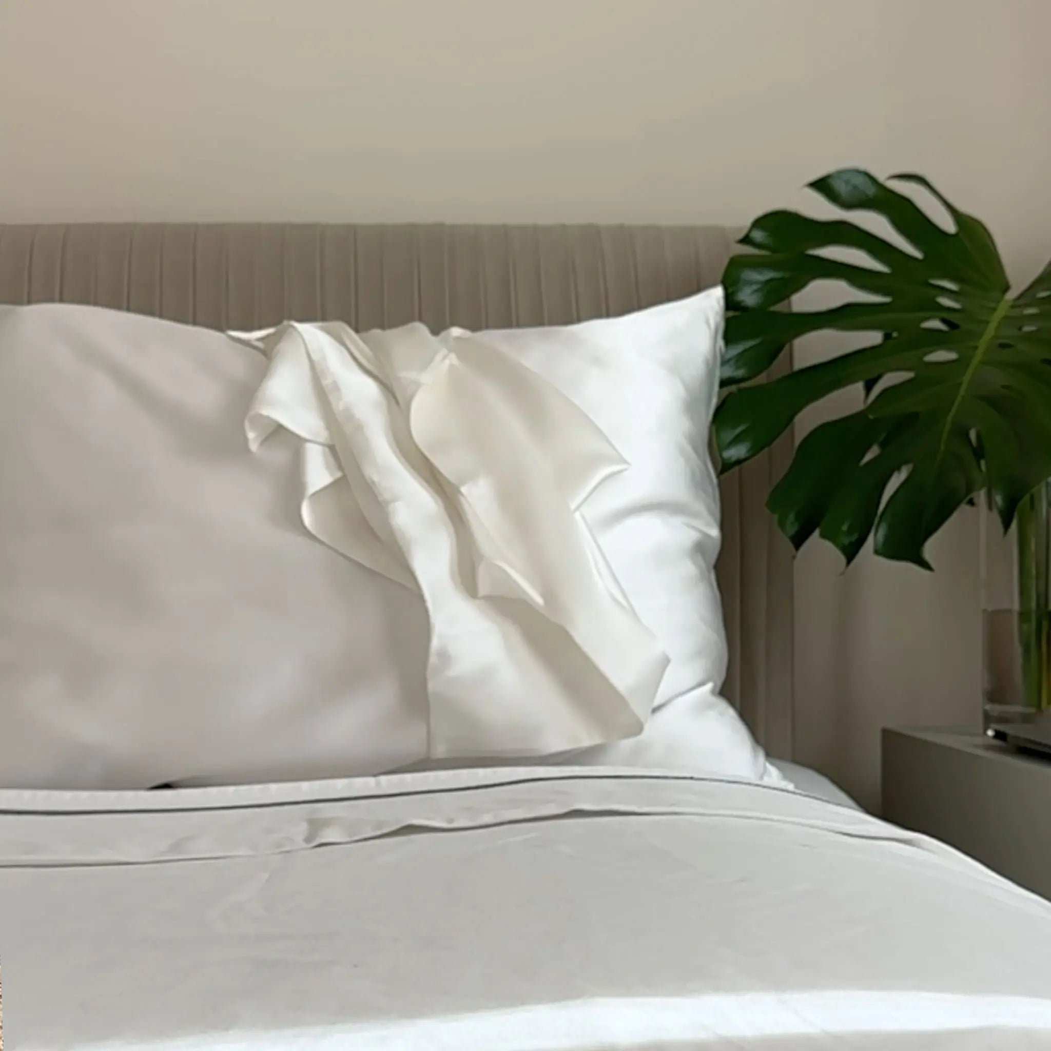 Neatly made bed with white bedding and pillows with Pure mulberry silk pillowcase in Ivory White color featuring a plant in the corner. — Silk Souq 22 momme luxury silk.