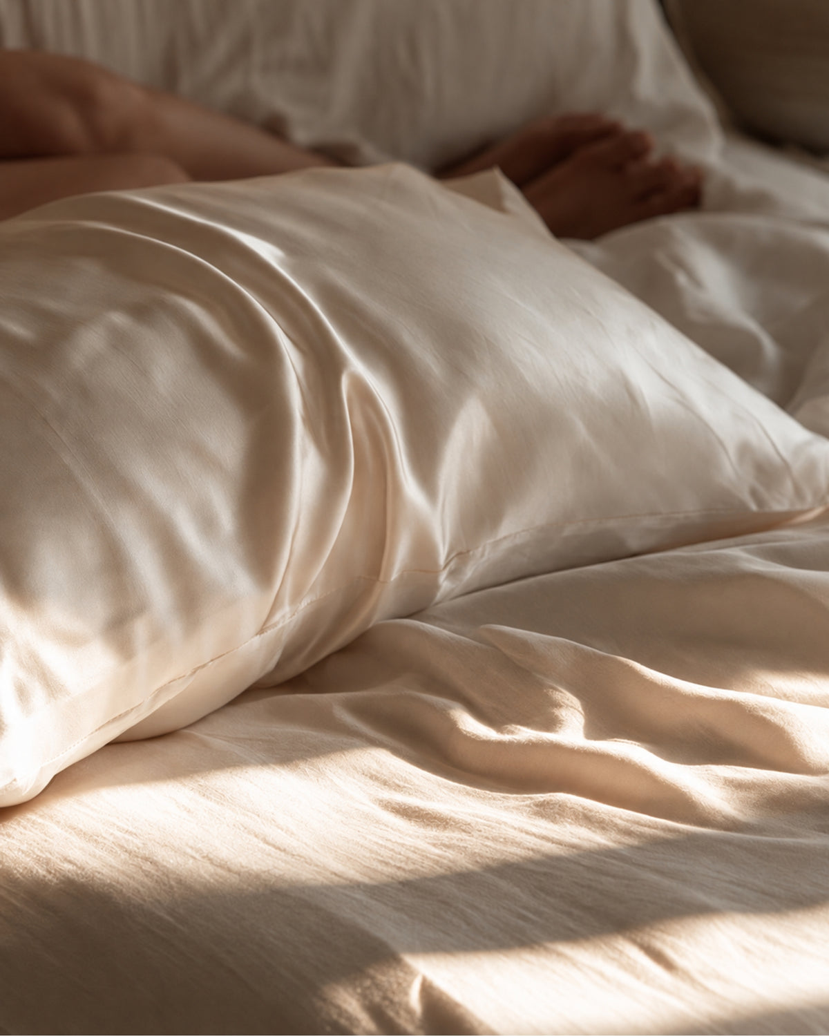 champagne color pure mulberry silk pillowcase on an oatmeal linen bed, softly lit by warm morning sunlight.